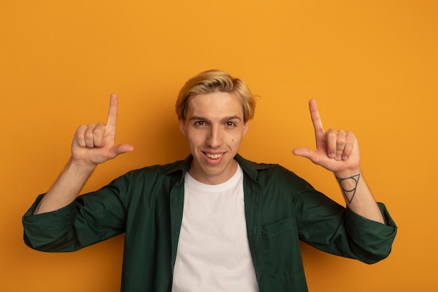 Smiling young blonde guy wearing green t-shirt points at up