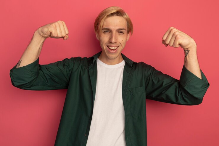Free Photo smiling young blonde guy wearing green t-shirt showing strong gesture