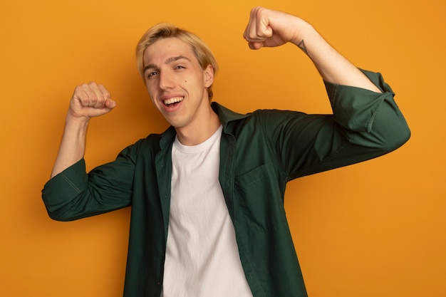 Smiling young blonde guy wearing green t-shirt showing strong gesture