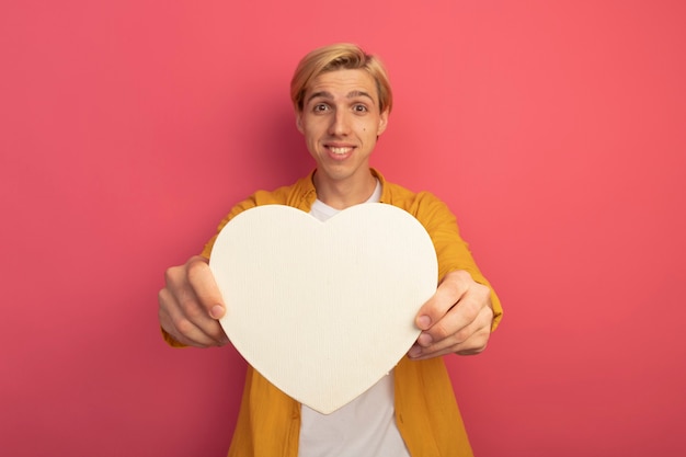 Giovane ragazzo biondo sorridente che indossa la maglietta gialla che tiene fuori la scatola di forma del cuore