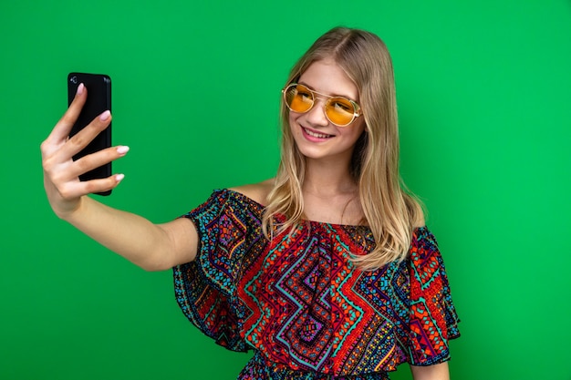 Smiling young blonde slavic girl with sun glasses holding and looking at phone