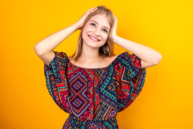 Smiling young blonde slavic woman putting hands on her head and looking up 
