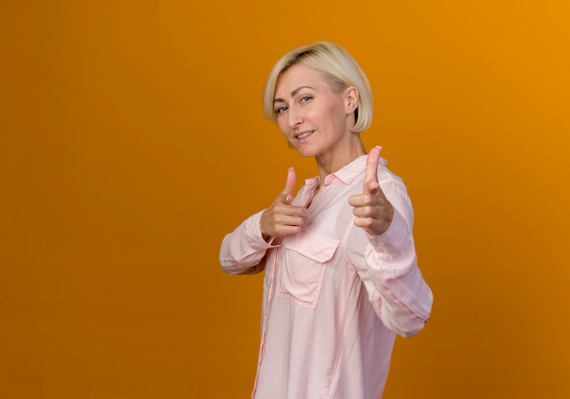 Smiling young blonde slavic woman showing you gesture isolated on orange with copy space