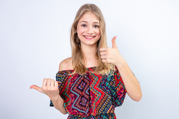 Smiling young blonde slavic woman thumbing up and pointing at side 