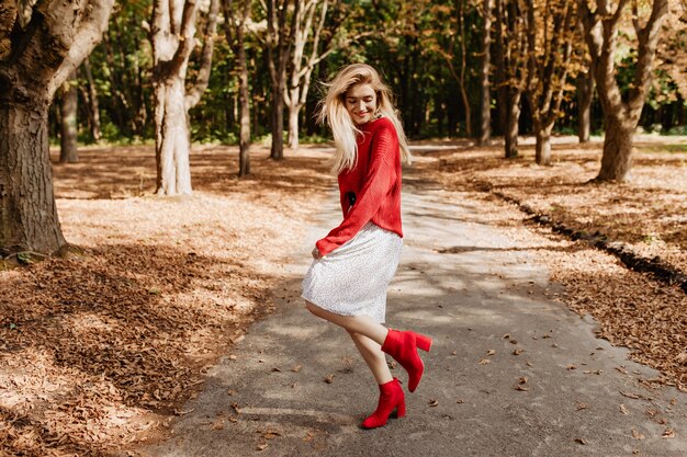 가 공원에서 재미 젊은 금발의여자가 웃 고. 세련된 빨간 구두와 하얀 드레스를 입고 춤을 춥니 다.