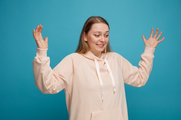 Smiling young blonde woman raising hands looking down 