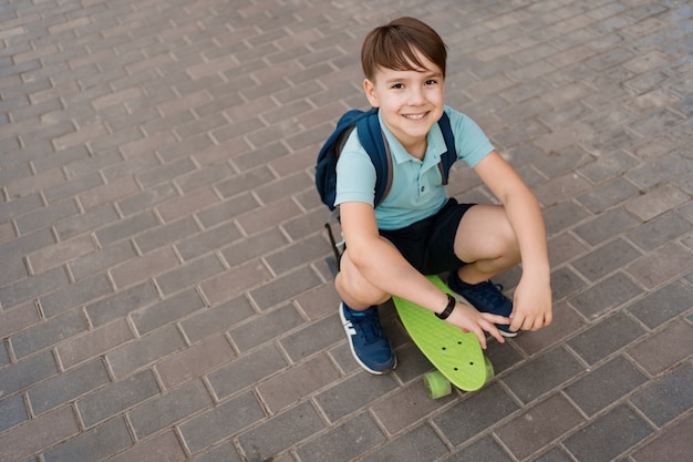 市内のスケートボード、ペニーボードに乗って白人の子供で遊ぶ少年の笑顔