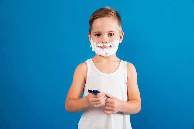 Smiling young boy in shaving foam holding razor