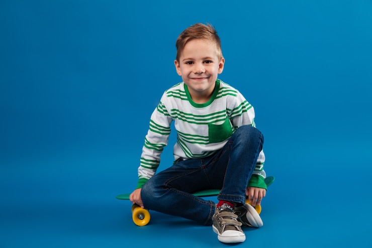 Free Photo smiling young boy sitting on skateboard and looking