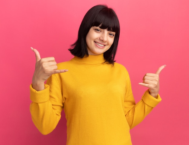Smiling young brunette caucasian girl doing hang loose gesture with two hands