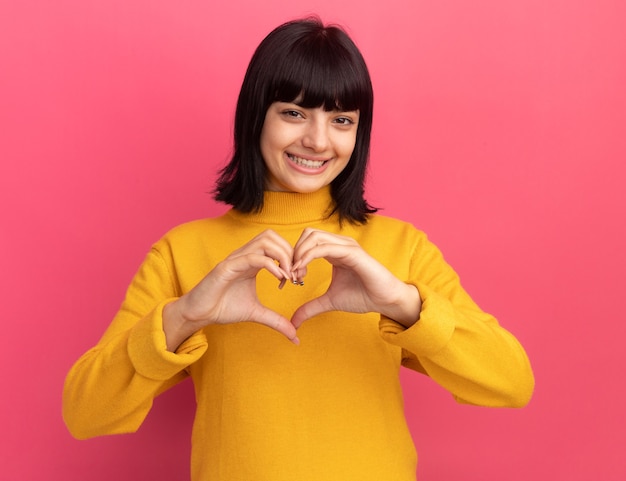 Smiling young brunette caucasian girl gestures heart sign