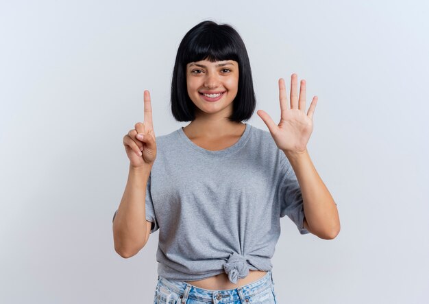 Smiling young brunette caucasian girl gestures six with fingers looking  