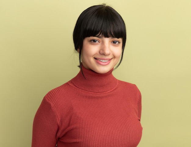 Smiling young brunette caucasian girl looks at camera on olive green