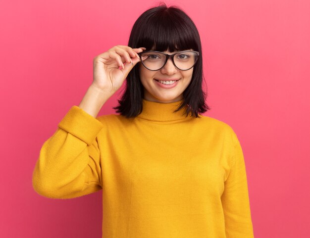 Smiling young brunette caucasian girl looks at camera through optical glasses