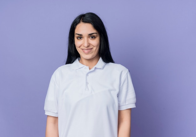 Smiling young brunette caucasian girl looks isolated on purple wall