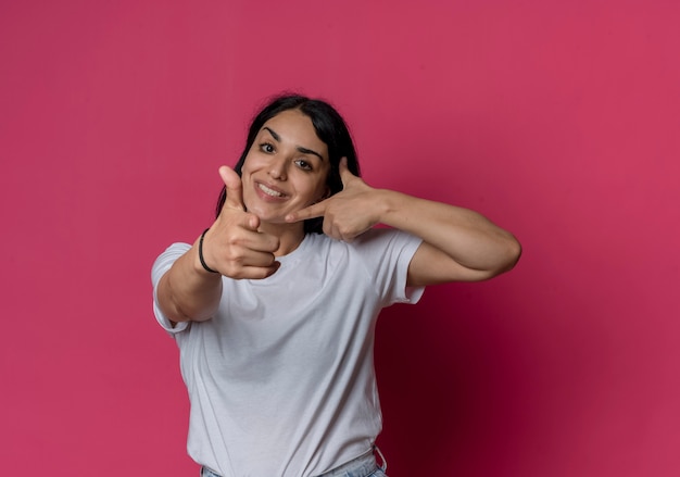 Sorridente giovane ragazza bruna caucasica punti e punti a lato isolato sulla parete rosa