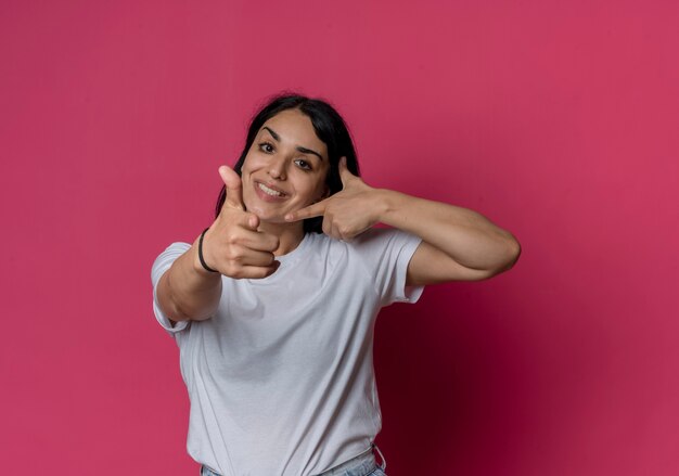 Smiling young brunette caucasian girl points and points at side isolated on pink wall