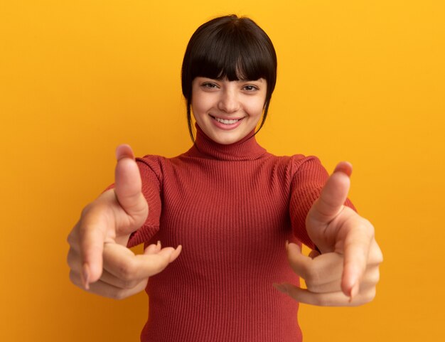 Улыбающаяся молодая брюнетка кавказская девушка указывает двумя руками, изолированными на оранжевой стене с копией пространства
