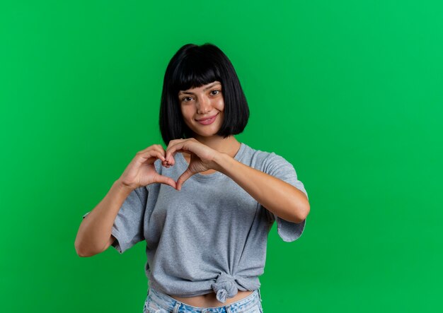 Smiling young brunette caucasian woman gestures heart hand sign