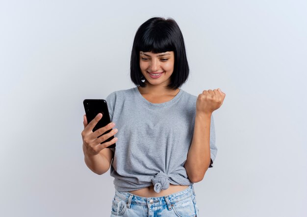 Smiling young brunette caucasian woman keeps fist looking at phone