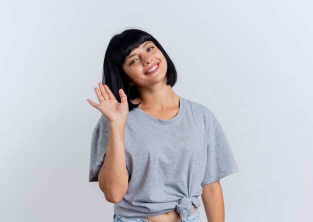 Smiling young brunette caucasian woman stands with raised hand