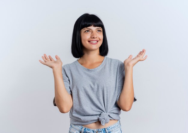 Smiling young brunette caucasian woman stands with raised hands looking at side