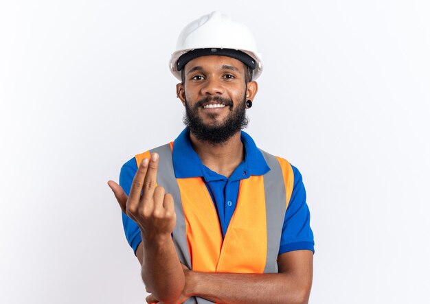 smiling young builder man in uniform with safety helmet calling someone with hand isolated on white wall with copy space