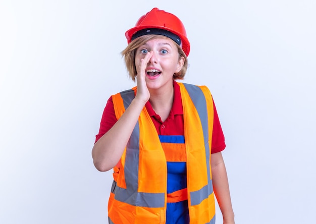 smiling young builder woman in uniform calling someone isolated on white wall