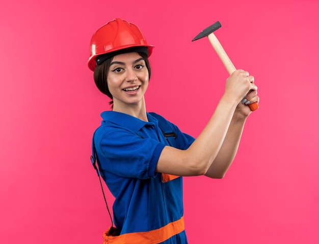 Smiling young builder woman in uniform raising hammer 