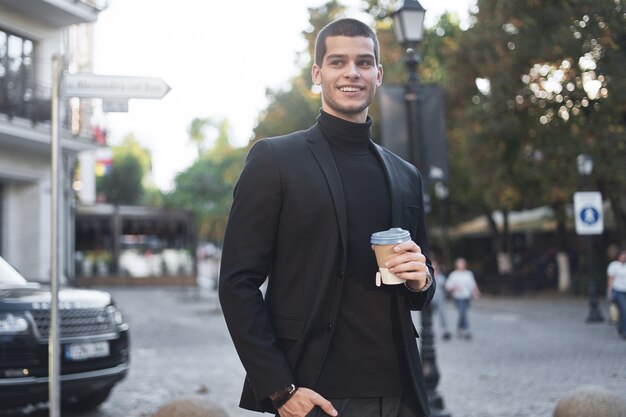 Улыбающийся молодой бизнесмен собирается на работу с кофе