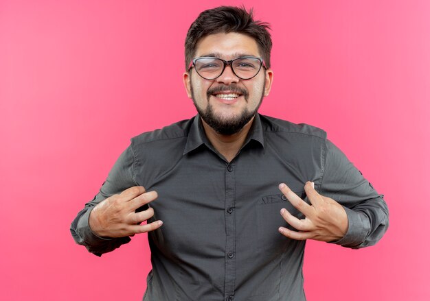 Smiling young businessman wearing glasses holding shirt isolated on pink wall