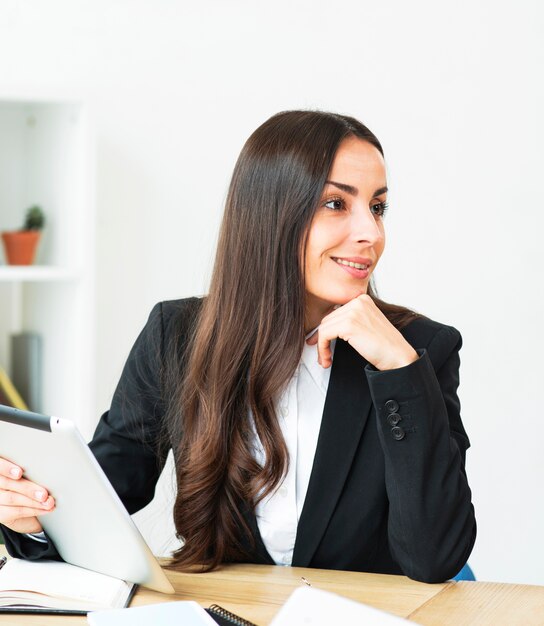 Smiling young businesswoman holding digital tablet in hand looking away