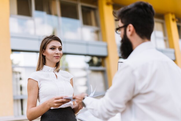 Smiling young businesswoman looking at businessman giving document to her