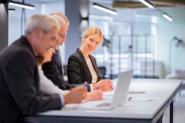 Smiling young businesswoman sitting with businesspeople working at workplace