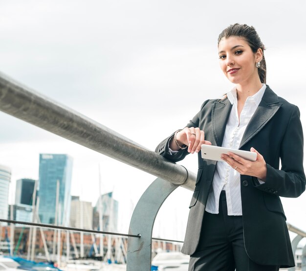 Smiling young businesswoman standing near the railing holding white mobile phone in hand