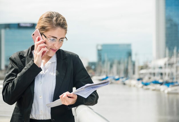 スマートフォンで話している手すりの近くに立っている笑顔の若い実業家