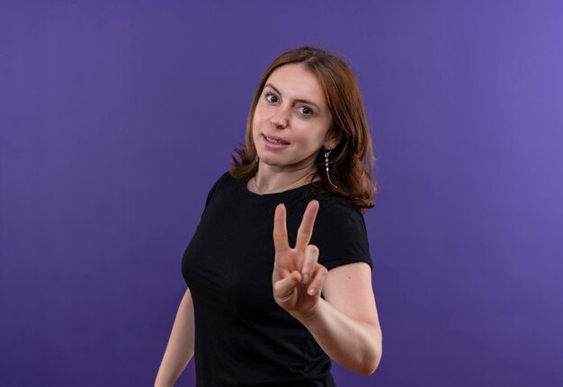 Smiling young casual woman doing peace sign on isolated purple space with copy space