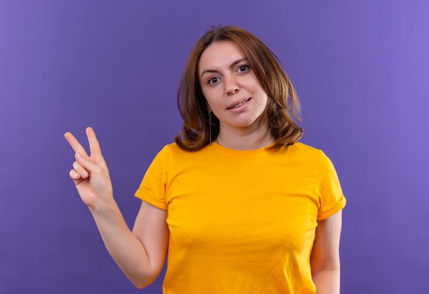 Smiling young casual woman doing peace sign on isolated purple space