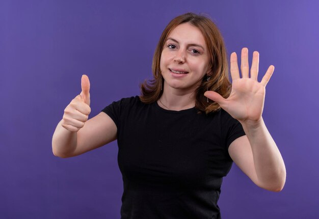 Улыбающаяся молодая случайная женщина, показывающая шесть на изолированном фиолетовом пространстве