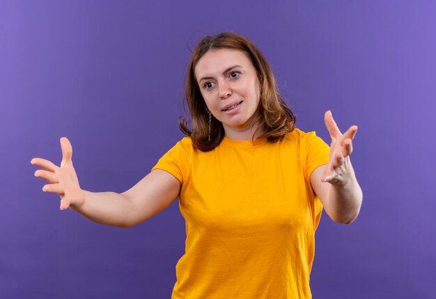 Smiling young casual woman stretching out hands on isolated purple space