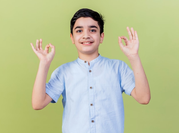 Smiling young caucasian boy  doing ok sign isolated on olive green wall