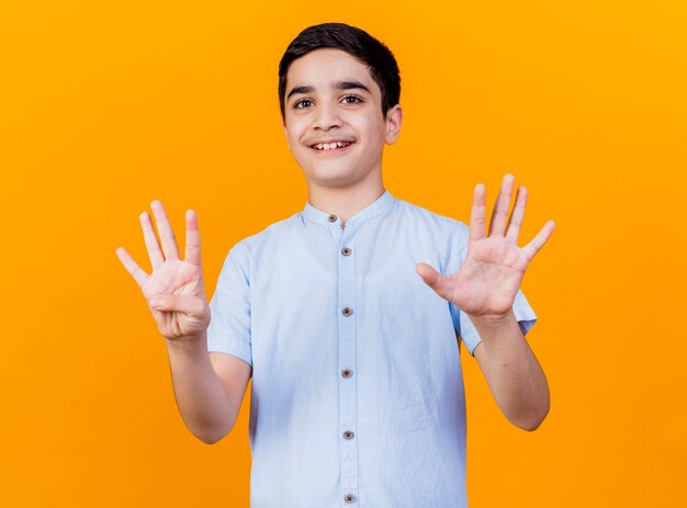 Smiling young caucasian boy looking at camera showing nine with hands isolated on orange background