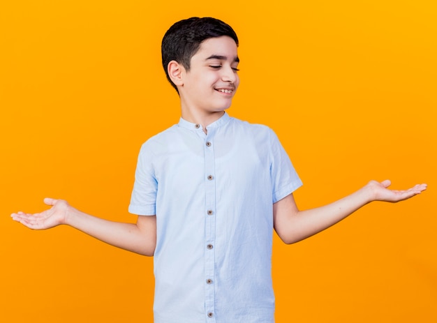 Smiling young caucasian boy showing empty hands looking at them isolated on orange background