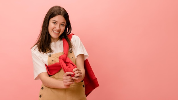 Smiling young caucasian brunette girl in casual clothes looks at camera on pink background with place for text Leisure lifestyle and beauty concept