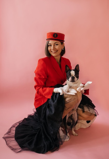 Smiling young caucasian brunette woman in red with her pet at photo shoot on pink background Love between dog and owner concept