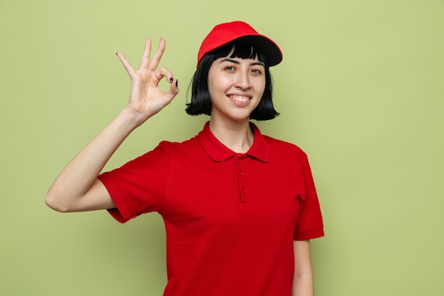 Smiling young caucasian delivery girl gesturing ok sign