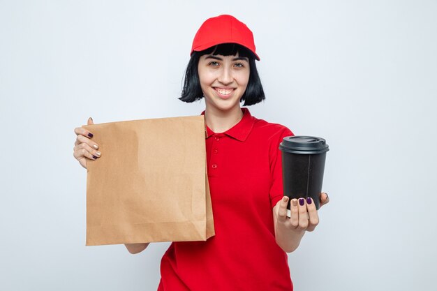 Smiling young caucasian delivery girl holding food packaging and paper cup looking at front