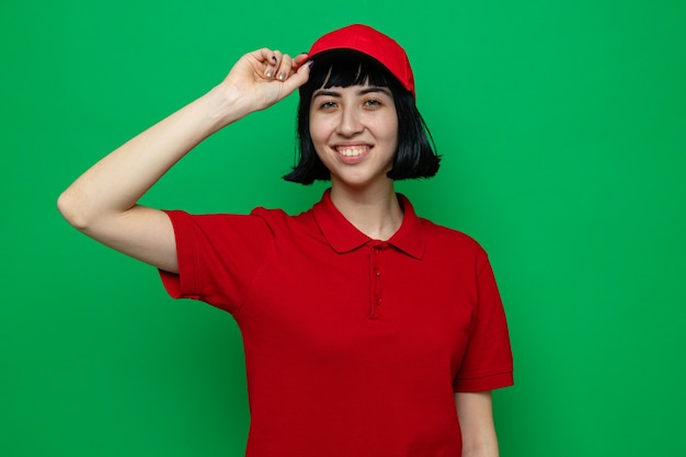 Smiling young caucasian delivery girl holding her cap and 