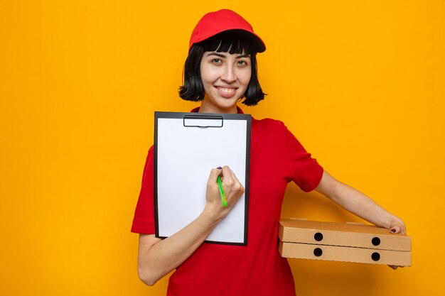 Smiling young caucasian delivery girl holding pizza boxes and clipboard