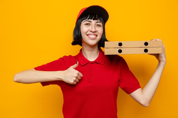 Free photo smiling young caucasian delivery girl holding pizza boxes on her shoulder and thumbing up